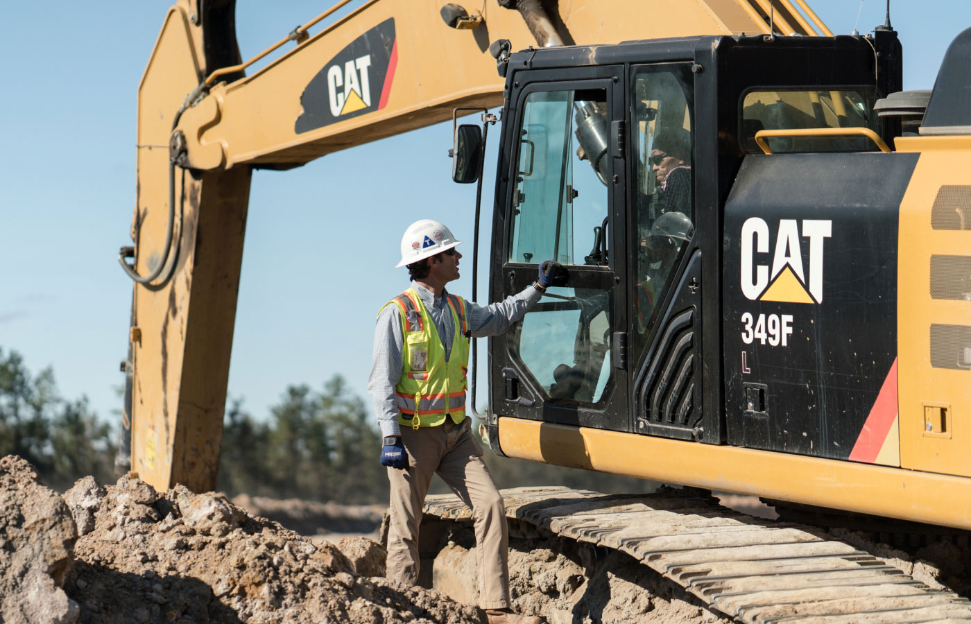 Heath C. Hanna In A Hard Hat & Neon Vest Talking With Contour Team Member Operating A Cat 349f At Mining Job Site