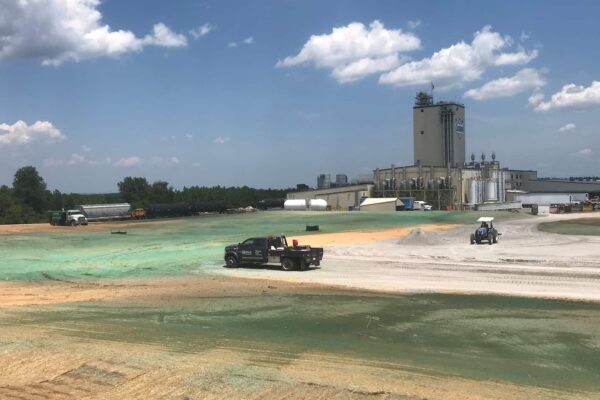 Large hydroseeded field next to an industrial plant with work vehicles and storage tanks on-site.