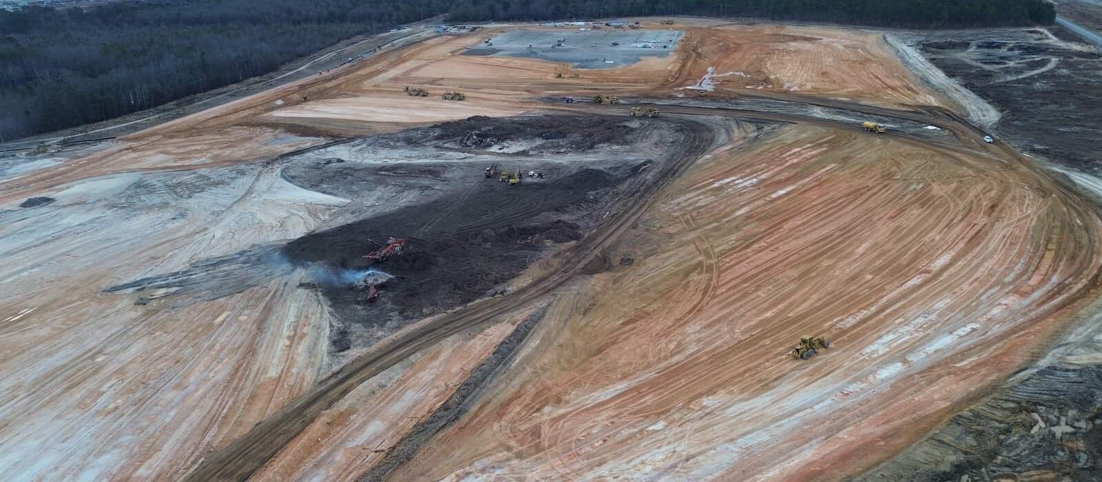 Aerial view of land clearing and grading operations at a large industrial site, with heavy equipment and cleared soil zones.