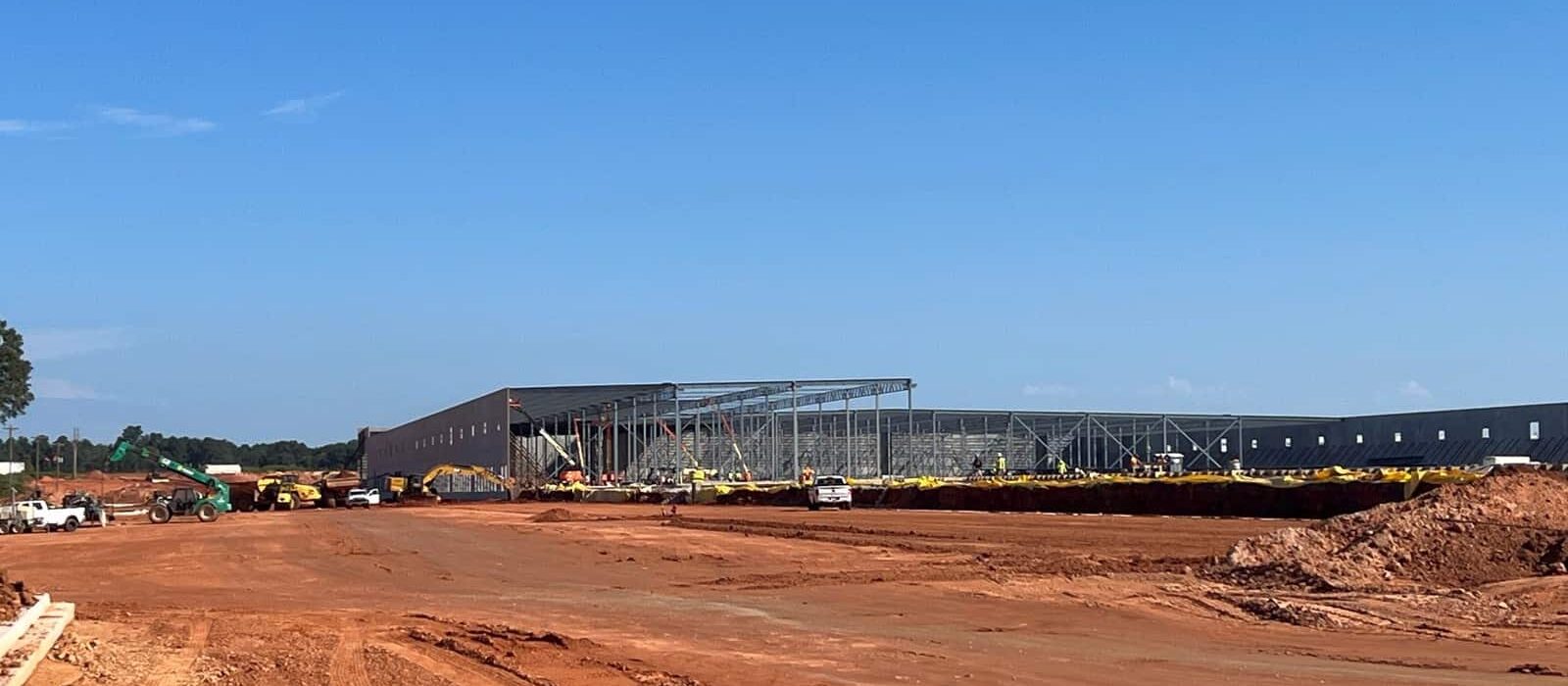 Wide view of a commercial construction site with steel framing underway for a large industrial warehouse building.
